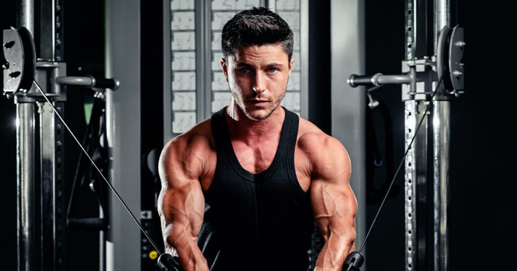 Frontal shot of a muscular man wearing a black tank top doing chest workout on cable machine